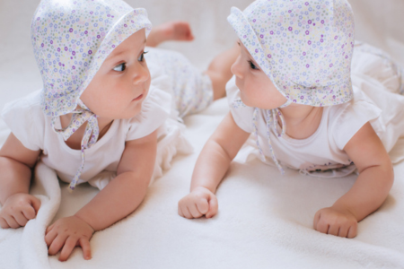 Två bebisar i likadana hattar ligger på mage och tittar på varandra
