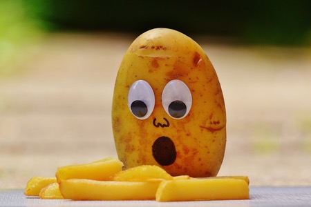 Rå potatis med påmålat ansikte som tittar på råa pommes frites.