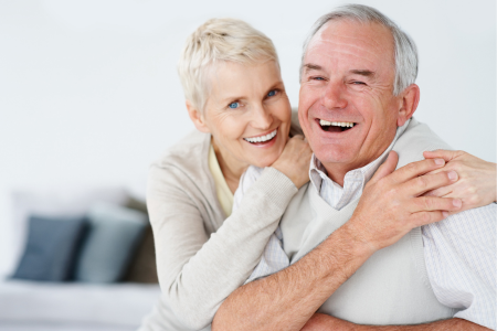 Två leende pensionärer klädda i vitt håller om varandra