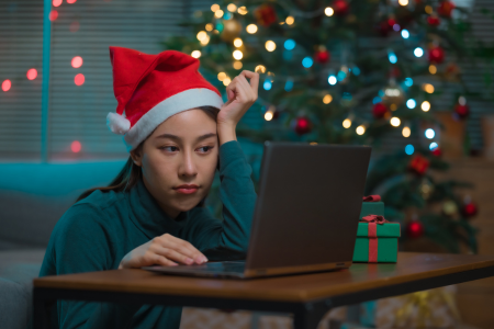 ledsen flicka i tomteluva sitter ensam framför en julgran med sin dator