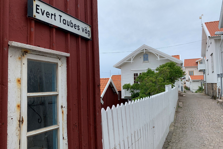 Kullerstensgata, hus, staket och sjöbodsvägg med gatuskylt för "Evert Taubes väg"