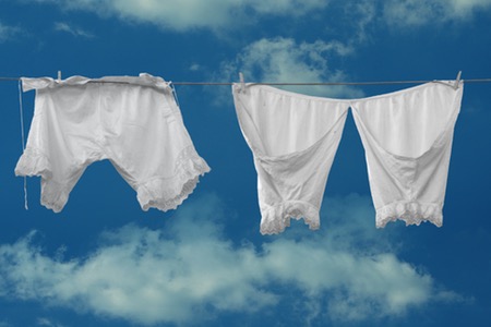 Gammeldags underkläder hänger på klädlina mot en blå himmel.