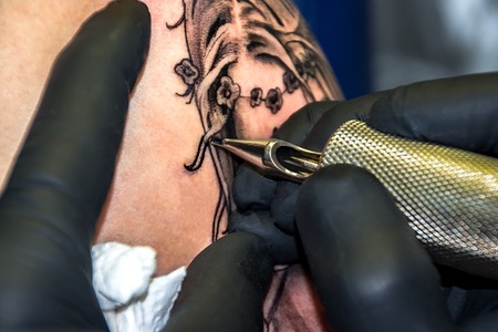 Hand håller tatueringsmaskin och gör tatuering för överarm.