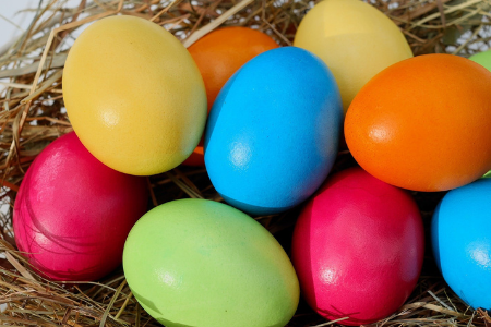 Målade ägg i skarpa färger ligger i ett hönsrede av halm.