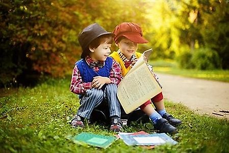 Två barn sitter utomhus med böcker.